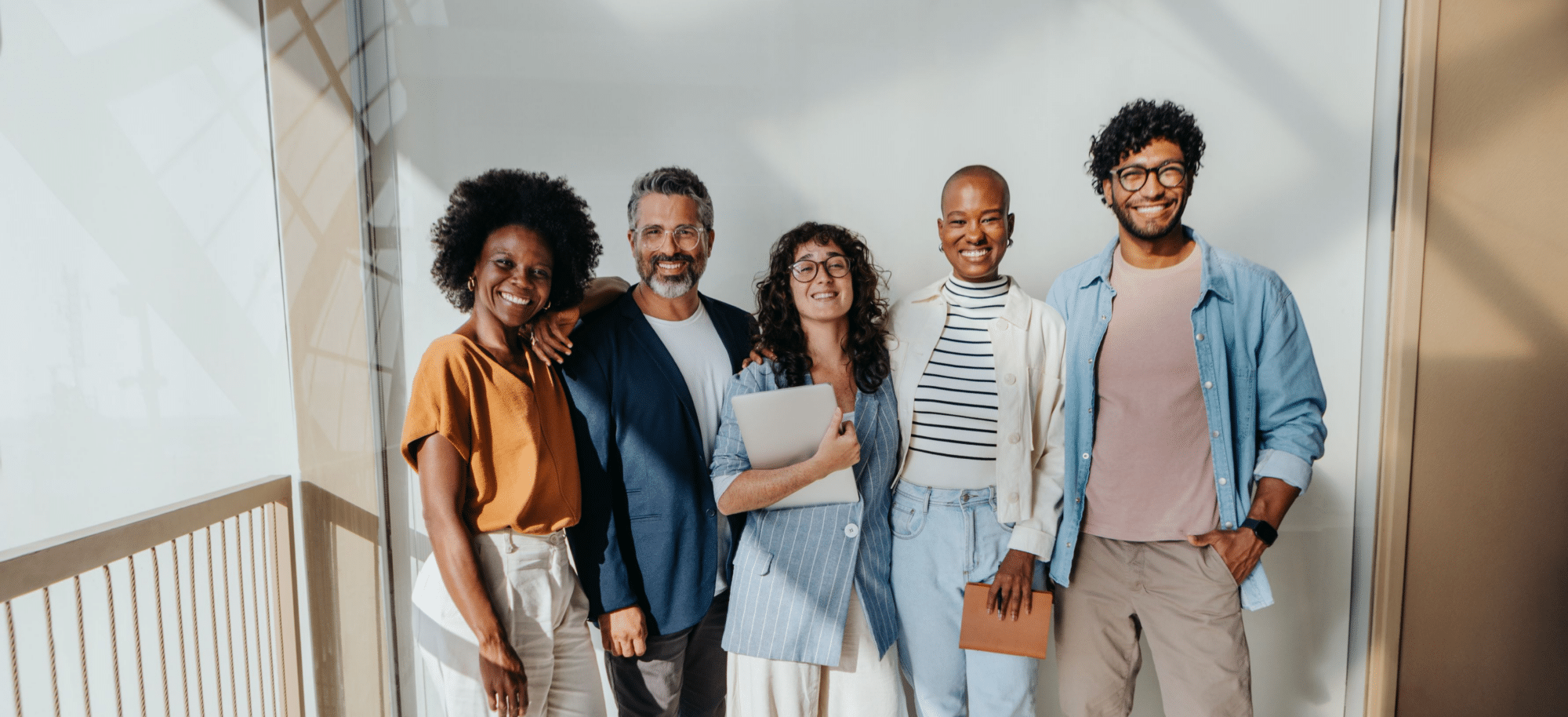 Group of diverse adults stanging in a birghtly lit hallway smiling.