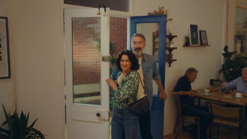 Freeze frame of a Specsavers TV advert. A middle-age couple arriving at a cafe smiling.